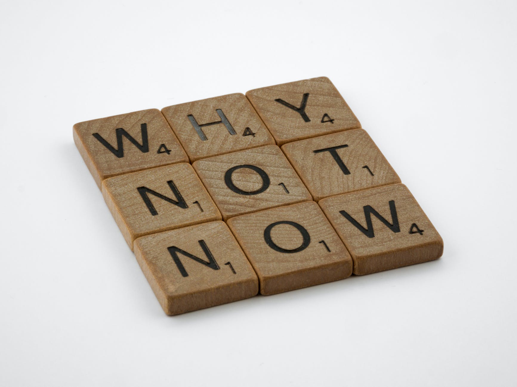 brown wooden blocks on white table spelling 'why not now' a good question to approach procrastination with!
